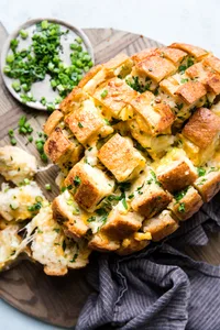 cheesy pull apart cheese bread topped with green onions  on a cutting board