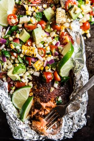 Salmon In Foil on a rimmed baking sheet with an Avocado Tomato and corn Salad with a fork