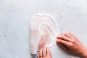 hands folding in edges of parchment paper to seal salmon in