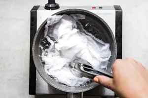 sauce pan of boiling water with tongs pushing down a tea towel to line the bottom