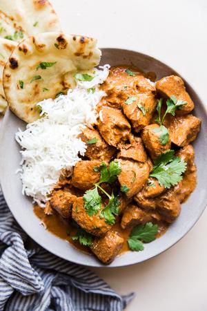 slow cooker butter chicken over white rice in a ceramic bowl served with naan and fresh cilantro