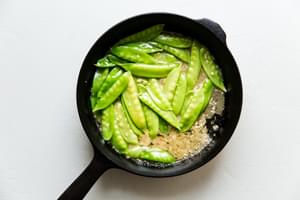 Garlic butter sauce simmering in a pan with snow peas.
