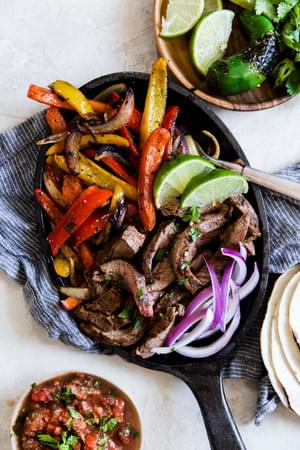 Steak Fajitas in a cast iron skillet with limes bell peppers and onions