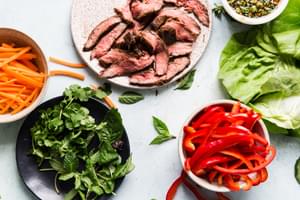 small plates with carrots, grilled sliced steak, fresh herbs and bell peppers laid out for steak lettuce cups