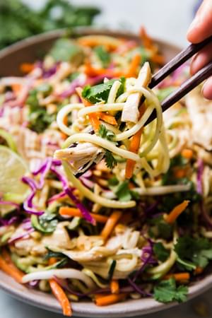 Thai Zucchini Noodle Salad being scooped up with wooden chop sticks from a bowl