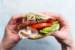 hand holding Turkey Bacon Club Sandwich with tomato avocado and pesto mayonnaise