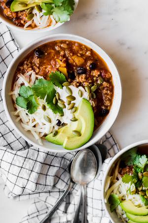 three bowls of turkey pumpkin chili topped with sour cream, cheese, avocado and fresh cilantro