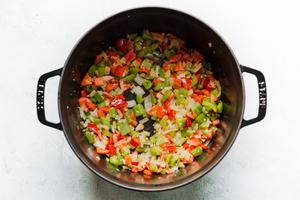 onions, peppers and garlic being cooked in olive oil in a large pot