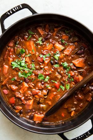 homemade vegetarian chili being stirred in a pot made with peppers, onion, sweet potatoes, beans, spices and enchilada sauce