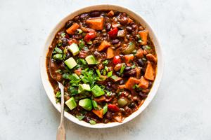 a bowl of homemade vegetarian chili made with bell pepper, sweet potato, onion and beans topped with avocado and green onions