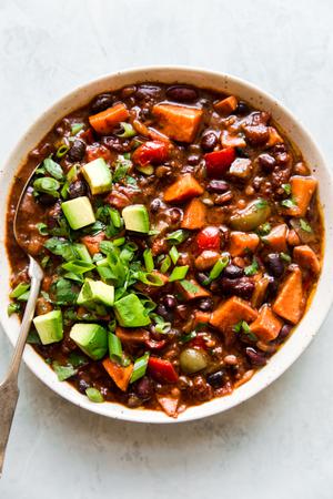 a bowl of homemade vegetarian chili made with bell pepper, sweet potato, onion and beans topped with avocado and green onions