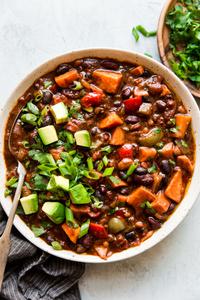 a bowl of homemade vegetarian chili made with bell pepper, sweet potato, onion and beans topped with avocado and green onions
