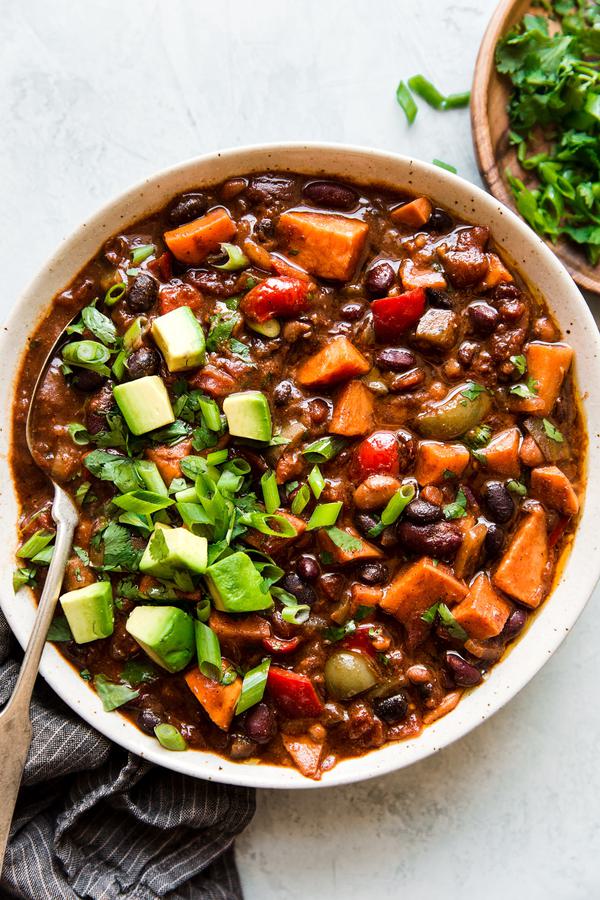a bowl of homemade vegetarian chili made with bell pepper, sweet potato, onion and beans topped with avocado and green onions
