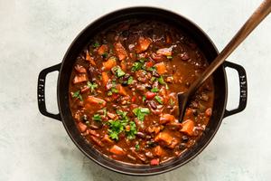 homemade vegetarian chili being stirred in a pot made with peppers, onion, sweet potatoes, beans, spices and enchilada sauce