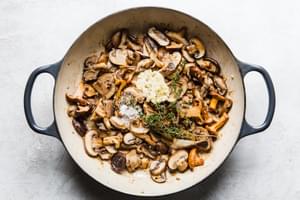 garlic, thyme, salt and pepper being added to a skillet of mushrooms and shallots that have been cooked in butter