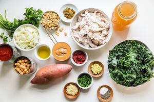 ingredients laid out for Peanut butter Soup onion, crushed tomatoes potatoes chickpeas, chicken, kale, peanuts and cilantro.