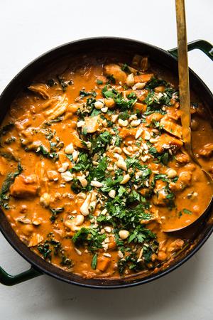 sweet and spicy peanut soup with chicken kale and sweet potatoes in a soup pot with a ladle. garnished with cilantro
