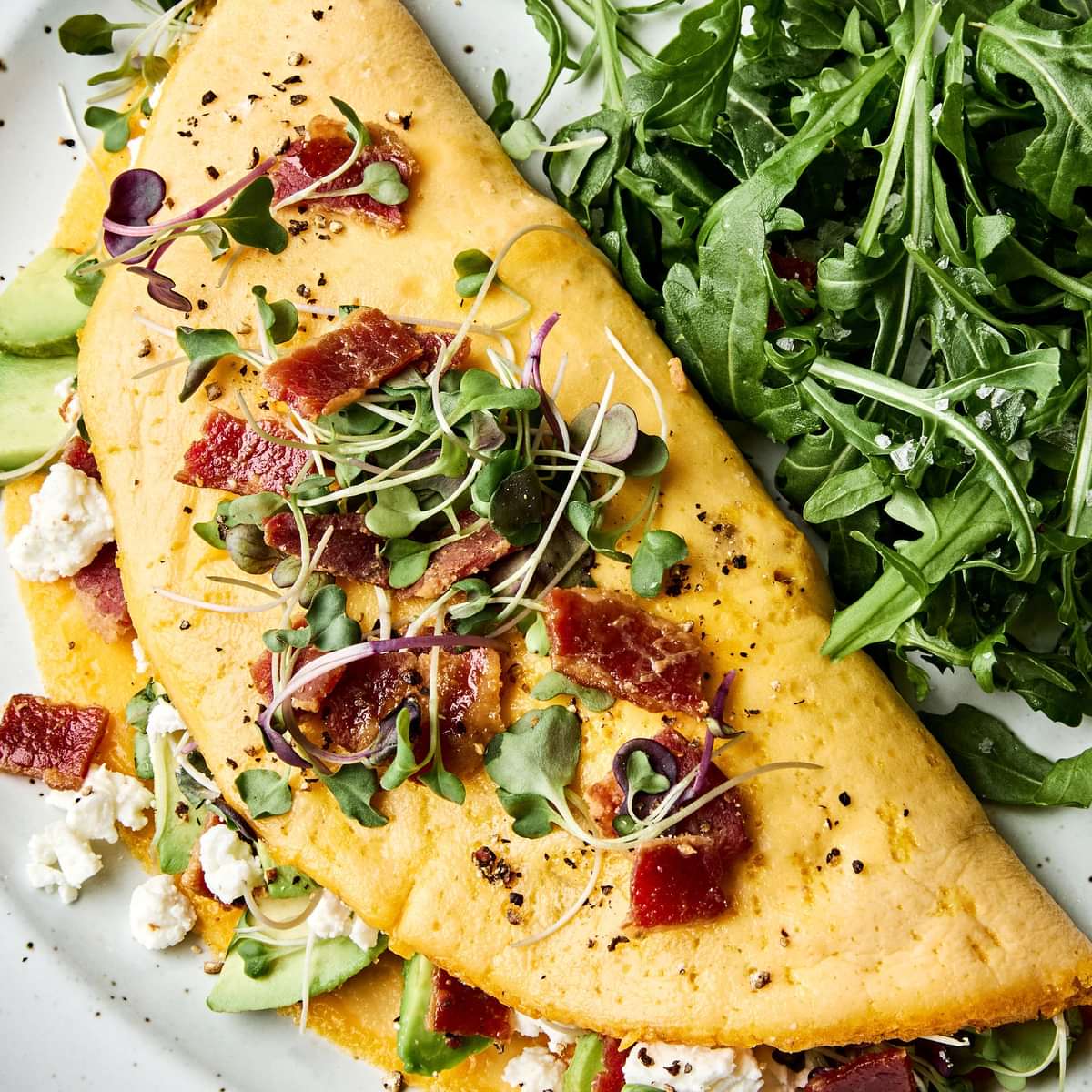 A bacon omelette with avocado and goat cheese topped with microgreens in a list of delicious breakfast ideas