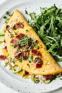 A bacon omelette with avocado and goat cheese topped with microgreens in a list of delicious breakfast ideas