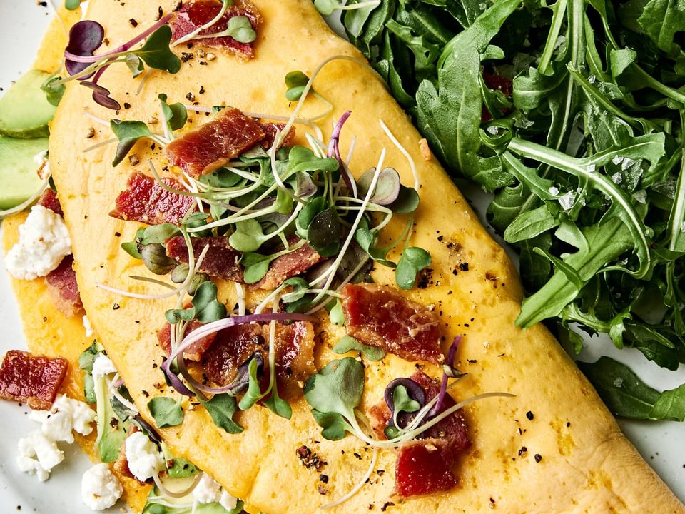 A bacon omelette with avocado and goat cheese topped with microgreens in a list of delicious breakfast ideas