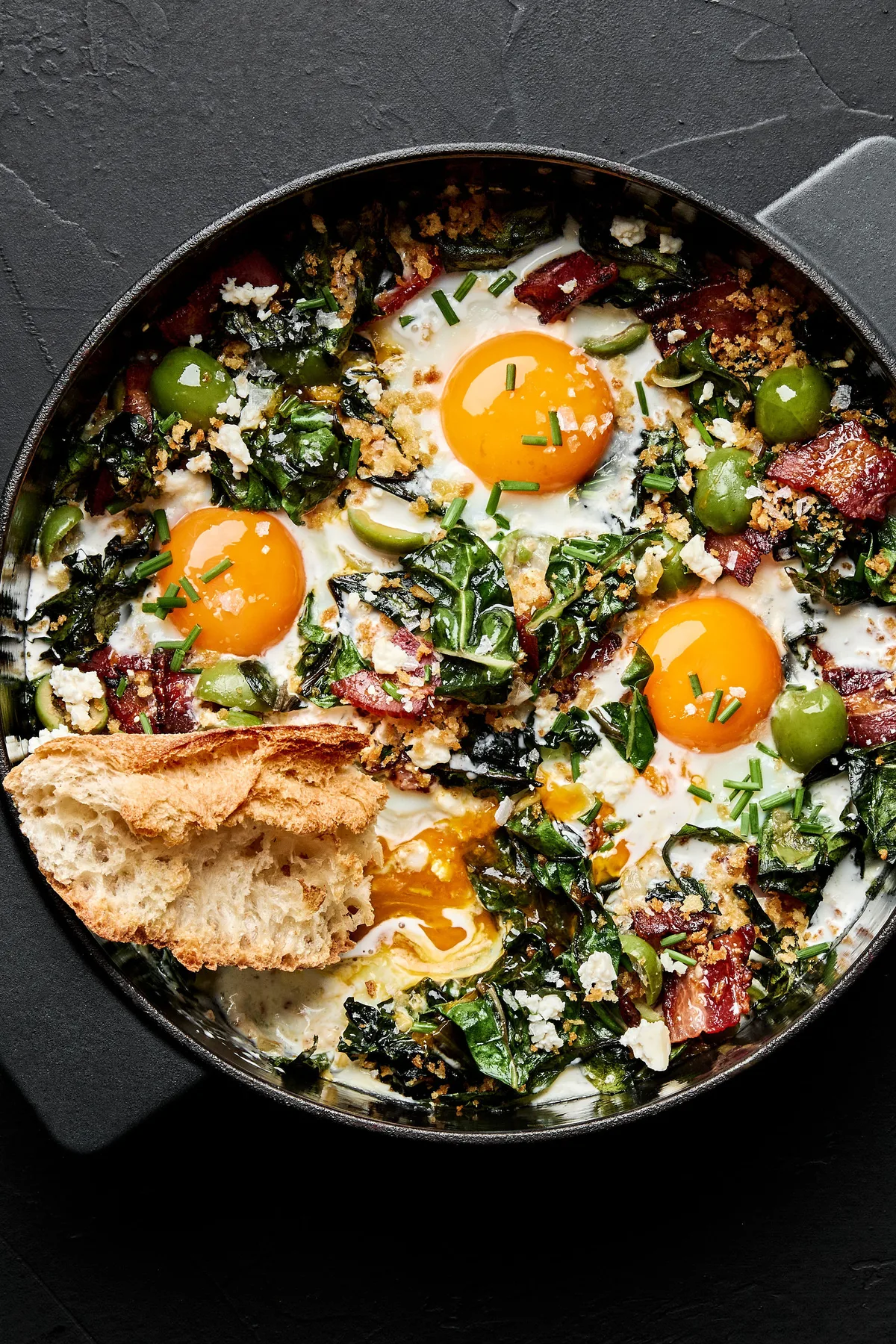 Baked eggs with swiss chard and green olives in a baking dish served with bread in a list of healthy breakfast recipes