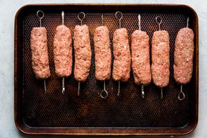 raw beef kofta skewers getting ready to be grilled on a sheet pan