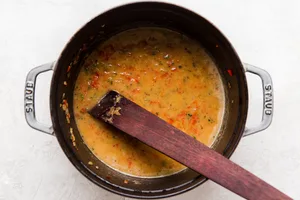 wooden spoon stirring jalapeño red bell peppers and onions with beer and stock