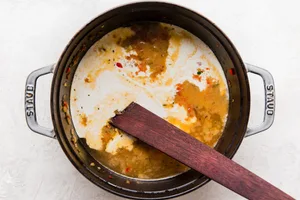 wooden spoon stirring jalapeño red bell peppers and onions with beer and stock and cream