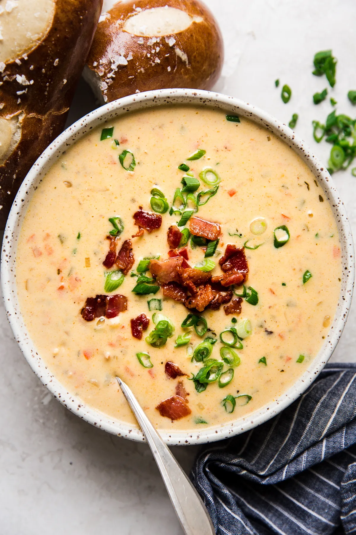 Beer Cheese Soup with bacon, peppers in a bowl with pretzel rolls and a spoon