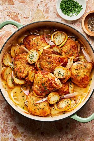 Braised chicken with potatoes and chive butter sauce in a braising dish with shallots and lemon
