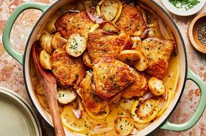 Braised chicken with potatoes and chive butter sauce in a braising dish being served with a wooden spoon