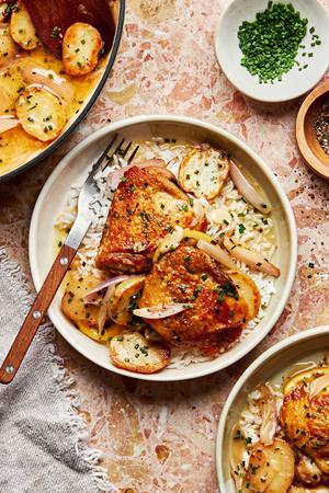 A serving of braised chicken with potatoes and chive butter sauce on top of rice in a bowl with a fork