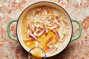 chicken stock being poured into a skillet with cooked shallots and garlic