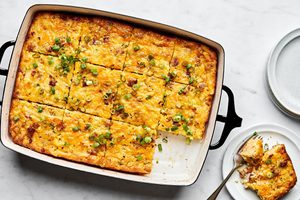 Breakfast casserole with hash browns, ground sausage, eggs, cream, and melted cheese topped with green onions