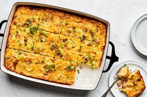 Breakfast casserole with hash browns, ground sausage, eggs, cream, and melted cheese topped with green onions