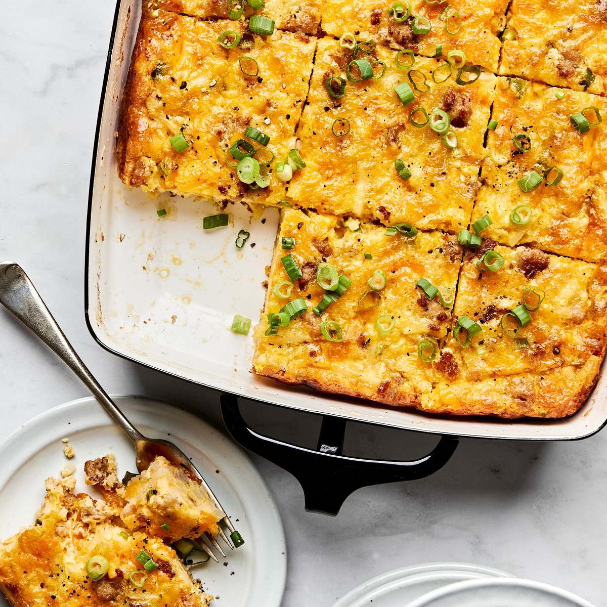Breakfast casserole with hash browns, ground sausage, eggs, cream, and melted cheese topped with green onions