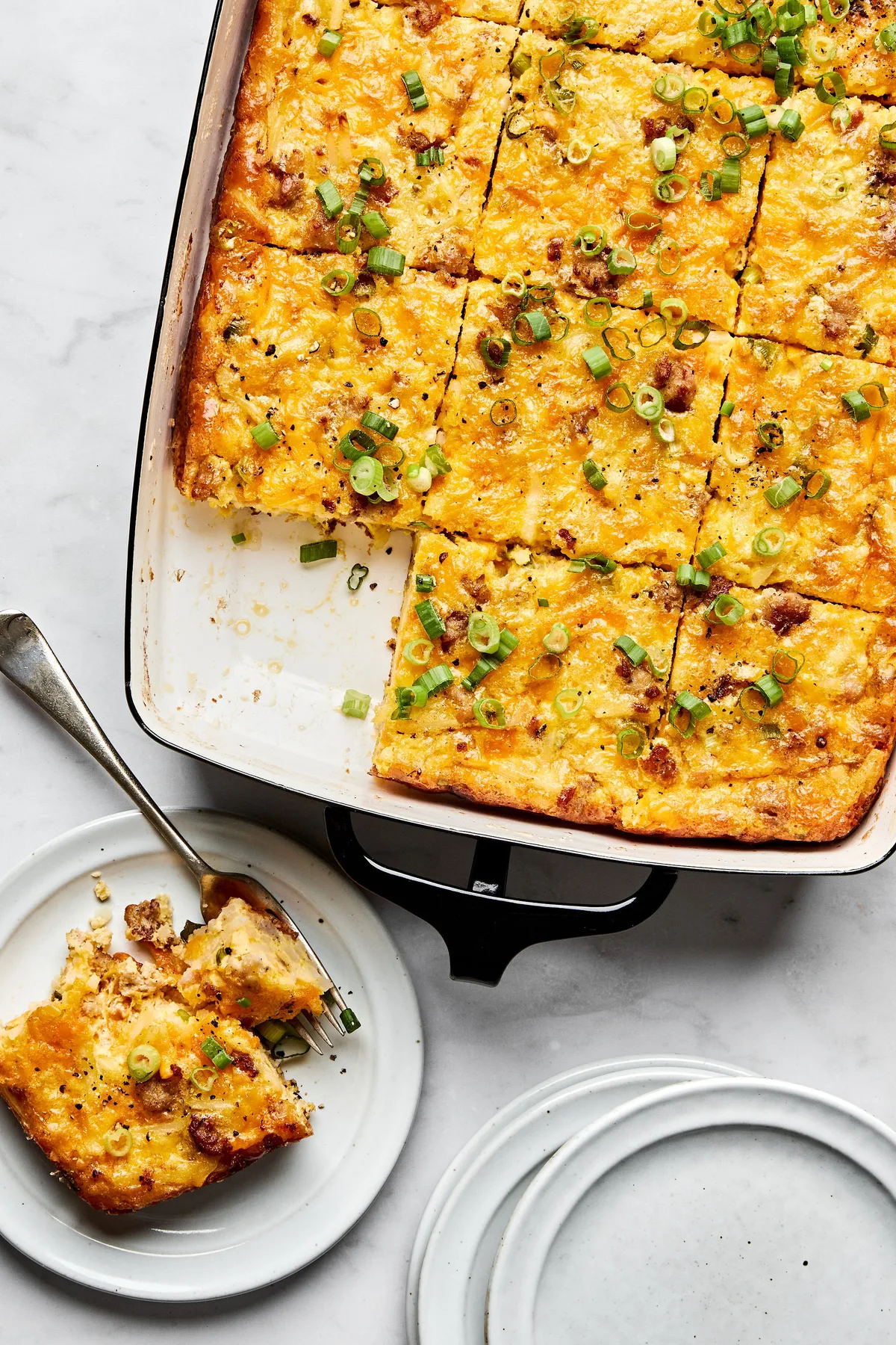 Breakfast casserole with hash browns, ground sausage, eggs, cream, and melted cheese topped with green onions