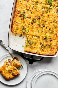 Breakfast casserole with hash browns, ground sausage, eggs, cream, and melted cheese topped with green onions