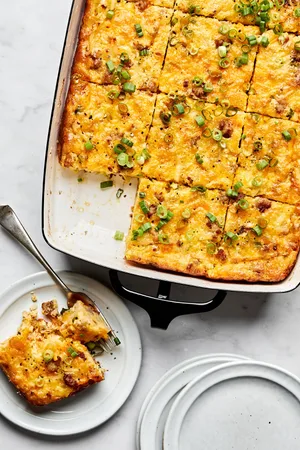 Breakfast casserole with hash browns, ground sausage, eggs, cream, and melted cheese topped with green onions