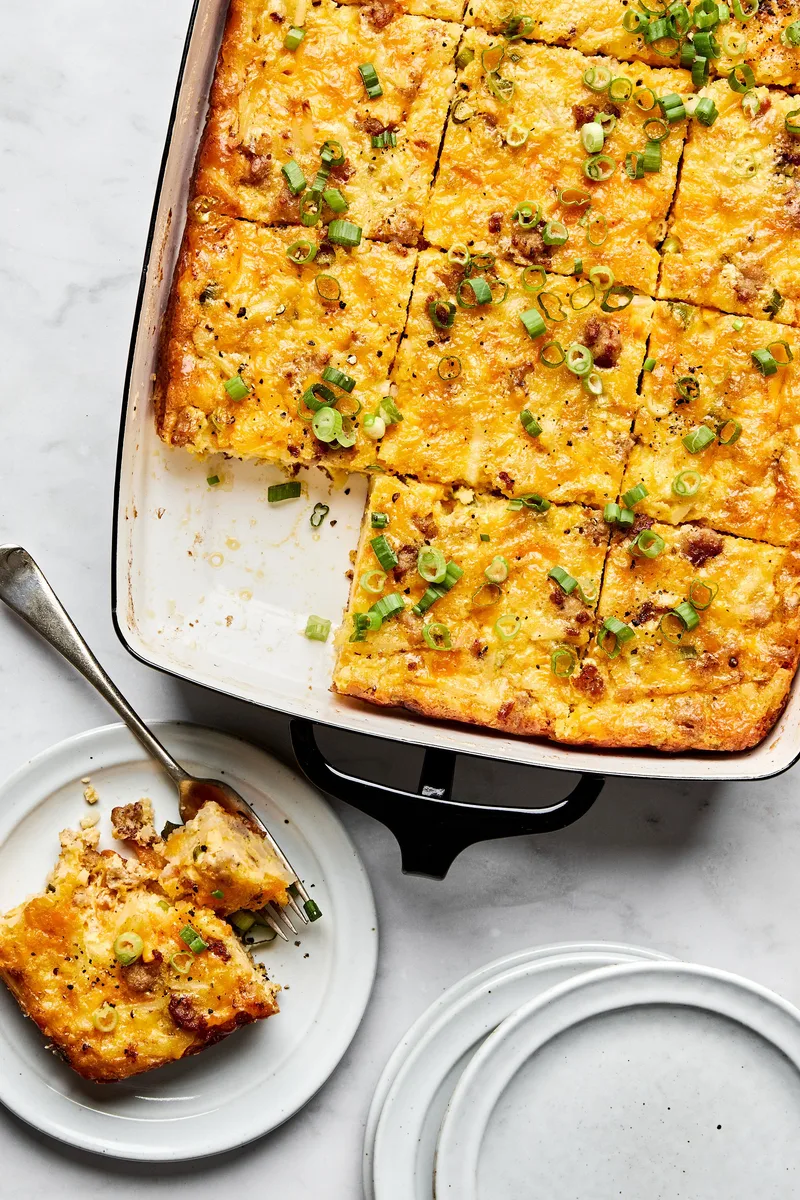 Breakfast casserole with hash browns, ground sausage, eggs, cream, and melted cheese topped with green onions