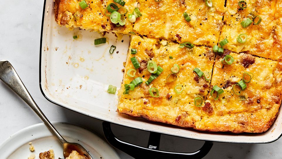 Breakfast casserole with hash browns, ground sausage, eggs, cream, and melted cheese topped with green onions