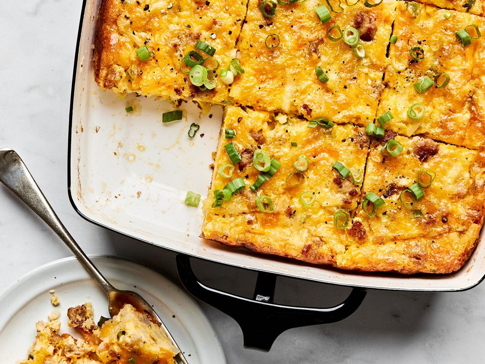 Breakfast casserole with hash browns, ground sausage, eggs, cream, and melted cheese topped with green onions