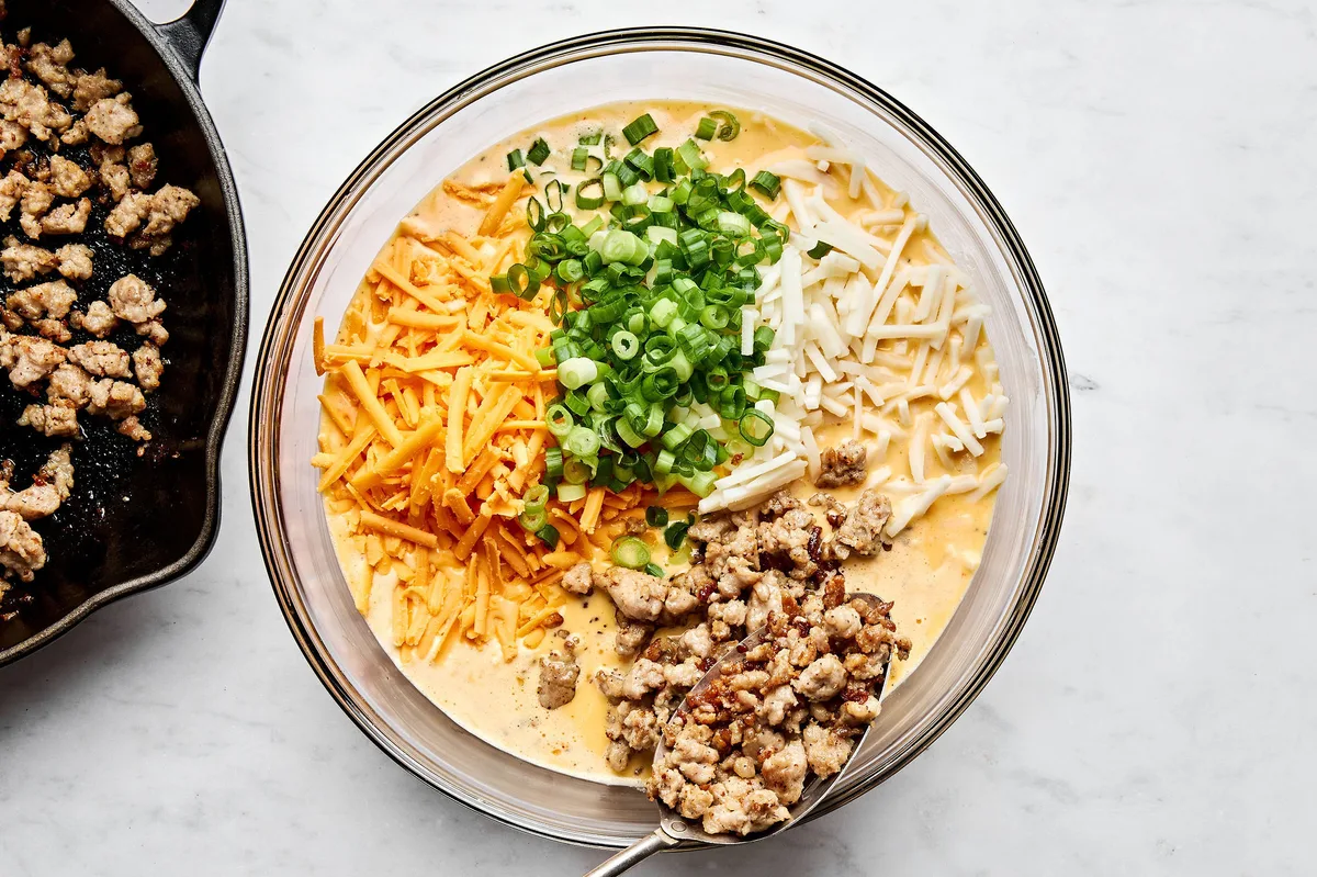 ingredients for breakfast casserole being stirred in a bowl: hash browns, eggs, sausage, cream, cheese and green onion
