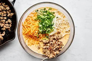 ingredients for breakfast casserole being stirred in a bowl: hash browns, eggs, sausage, cream, cheese and green onion