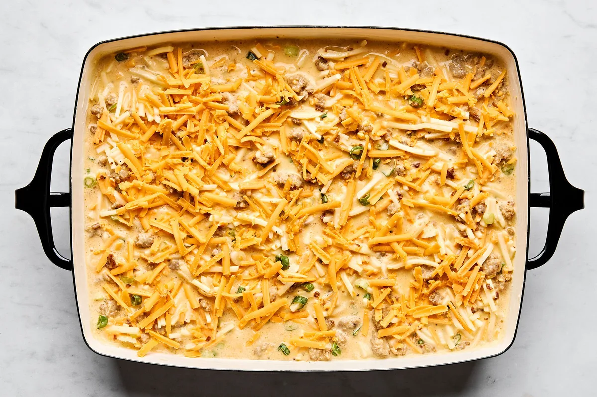 Unbaked breakfast casserole with hash browns, sausage, eggs, cream, and cheese, ready to go in the oven
