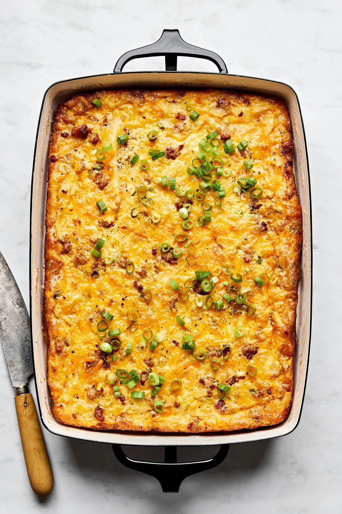 Breakfast casserole with hash browns, ground sausage, eggs, cream, and melted cheese topped with green onions