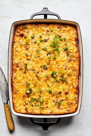 Breakfast casserole with hash browns, ground sausage, eggs, cream, and melted cheese topped with green onions