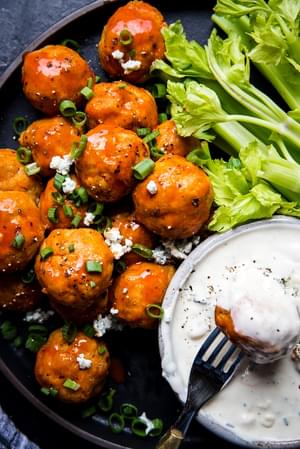 Buffalo chicken meatballs on a plate with a small bowl of blue cheese dressing and celery