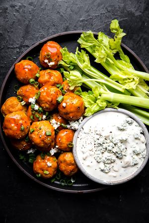 Buffalo chicken meatballs on a plate with a small bowl of blue cheese dressing and celery