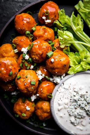 Buffalo chicken meatballs on a plate with a small bowl of blue cheese dressing and celery